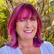 Claire Hennessy smiling with magenta shoulder length hair, white t-shirt, and outdoor background