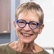 Sherry Norfolk smiling while wearing bright blue rimmed glasses and an olive green blouse