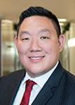 Johnny Wang smiling wearing a black suit coat with a red tie and white shirt