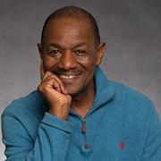 Bobby Norfolk smiling wearing a blue green shirt with his chin resting in his right hand