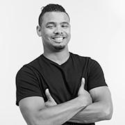 Justin Perez in black and white smiling with his arms crossed and thumbs up wearing a dark colored shirt