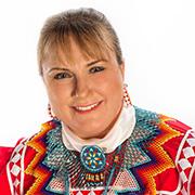 Suzanne Michelle Jones smiling wearing Native American attire in bright colors against a white background