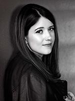 Black and white over the right shoulder photo of Alexandra Bracken with a small smile, long hair down and wearing a dark jacket