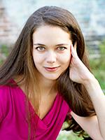 Jennifer Lynn Barnes smiling with her long brown hair parted on the right and left hand next to her left cheek while wearing a bright magenta top