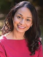 Makiia Lucier with her dark hair down, parted on the side and curled on the end with her hair over her left shoulder and wearing a bright magenta blouse 